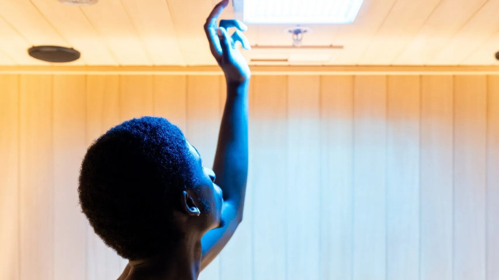 Man adjusts blue light in sauna for chromotherapy.